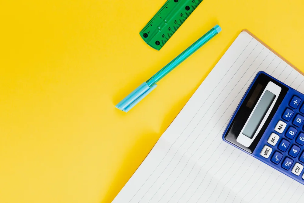Top view of educational stationery on a yellow background, featuring a calculator, notebook, and pen.