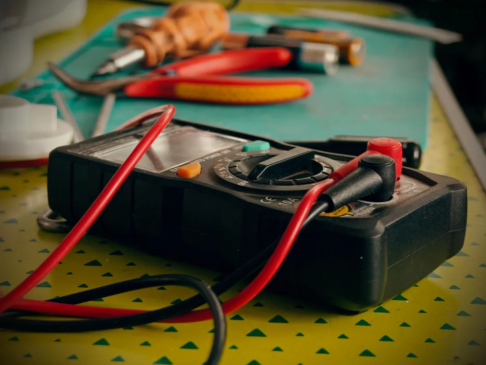 Close-up view of a multimeter and various tools on a workspace table.