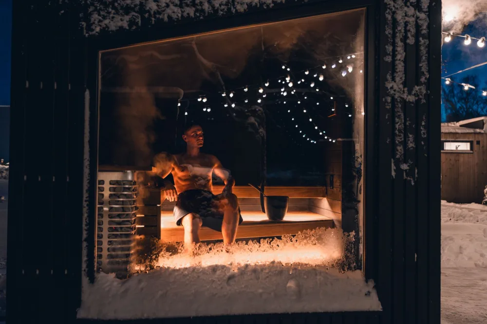 A man enjoys a relaxing evening in a snowy, warmly lit sauna, capturing a tranquil winter moment.