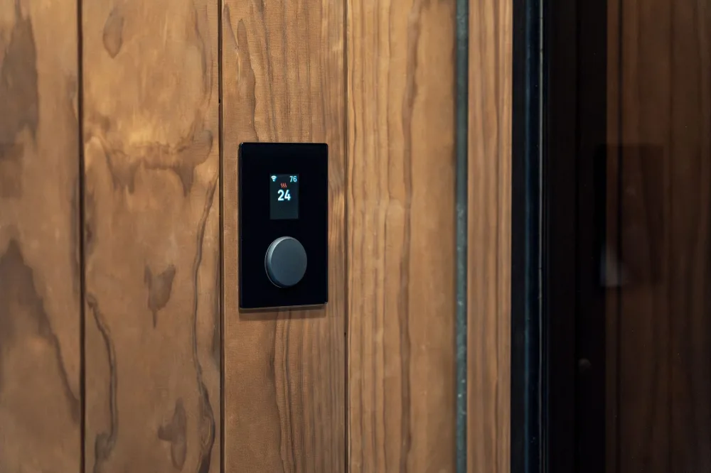 Close-up of a modern sauna control panel featuring a digital thermostat on a wooden wall, highlighting Scandinavian design.