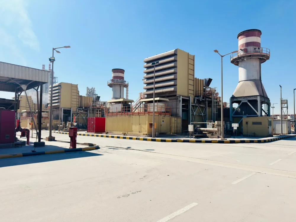 A modern power plant with turbines and chimneys under a clear blue sky in Saudi Arabia.