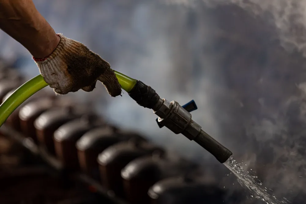 A gloved hand handling an industrial water hose with steam in the background.