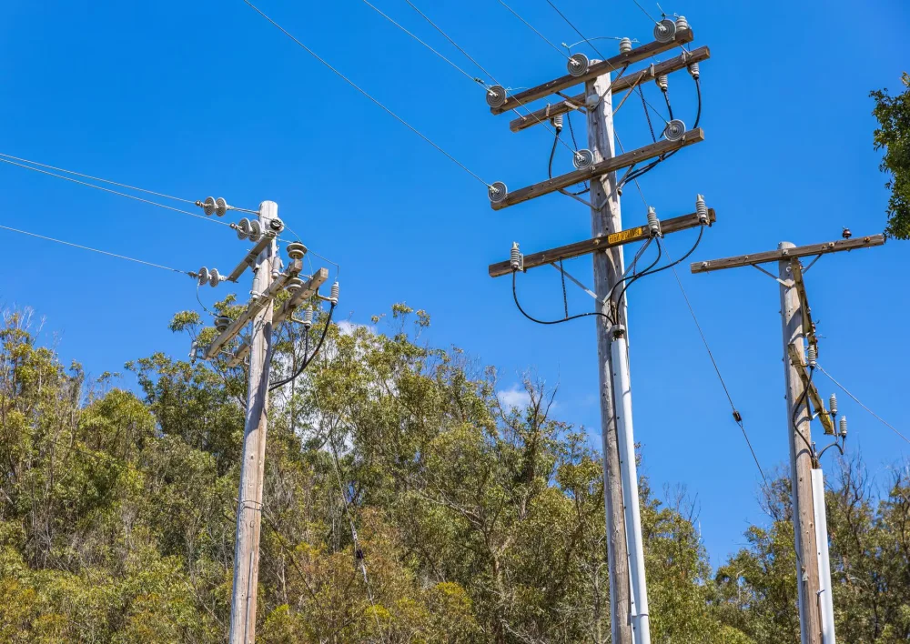 Wooden utility poles with power lines and a blue sky backdrop. Ideal for energy and utility themes.