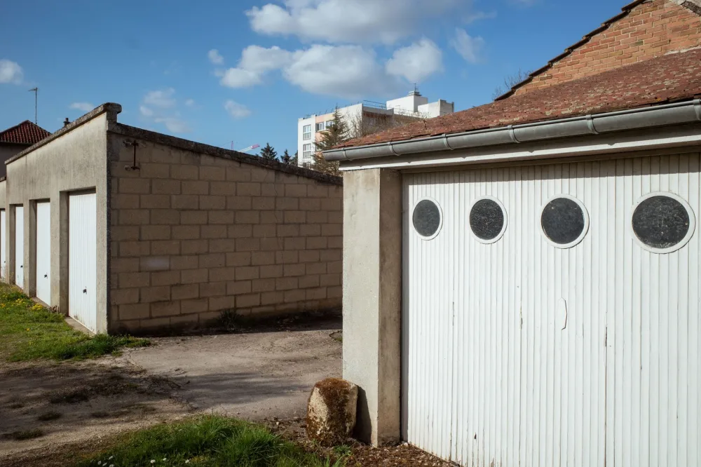 Series of garages with distinctive round windows under a clear blue sky in Compiègne, France.