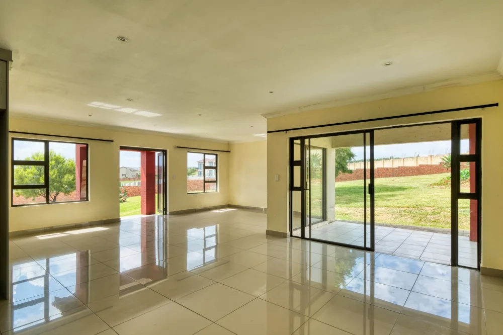 Bright and spacious empty living room in Pretoria with large windows, offering a view of the garden, ideal for real estate listings.