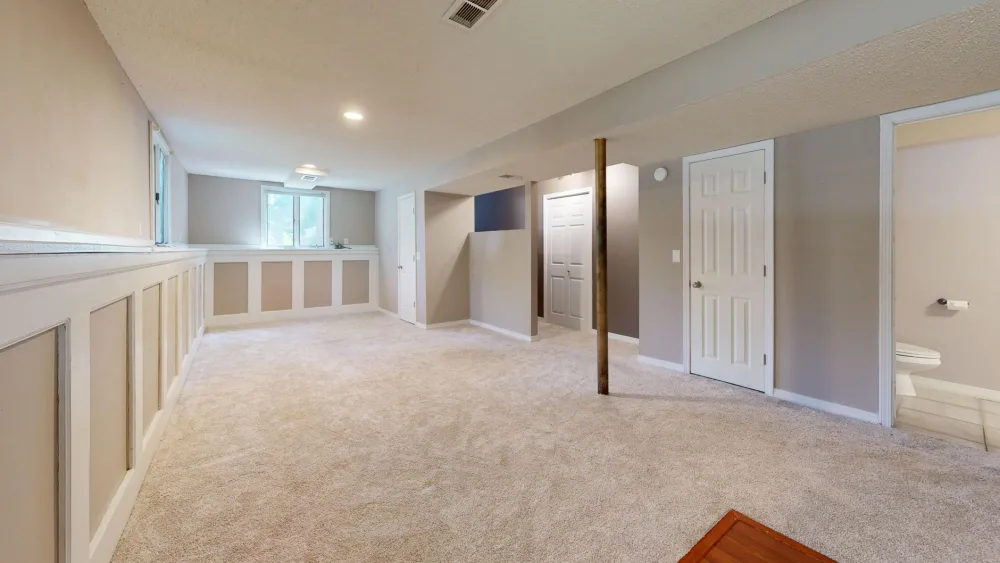 Bright and clean modern basement with carpet flooring and recessed lighting.