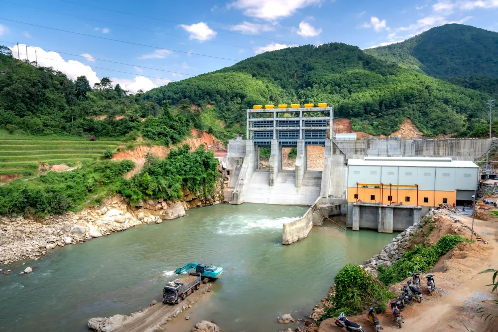 A hydroelectric dam nestled in a lush mountainous landscape under a bright daytime sky.