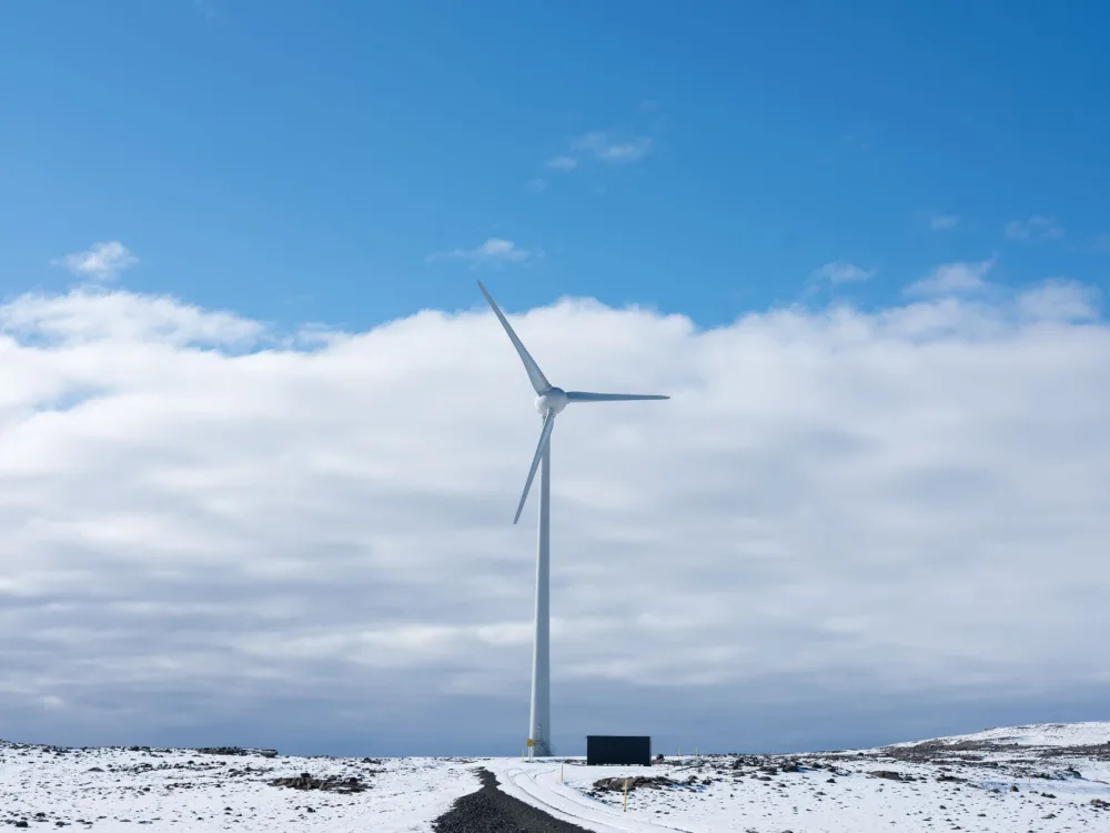 A wind turbine stands tall on a snowy landscape under a bright blue sky, symbolizing renewable energy.