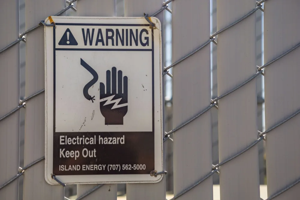 Close-up of a warning sign for electrical hazards on a chain-link fence.