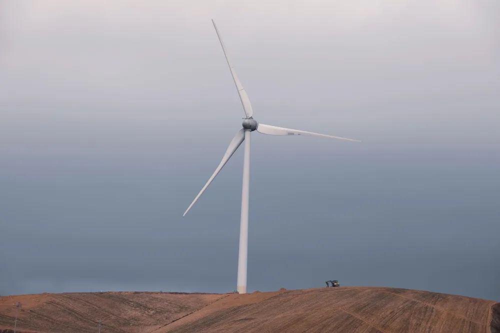 A large wind turbine on rolling hills against a cloudy sky, symbolizing renewable energy.